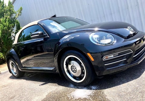 Black Volkswagen Beetle with white-wall tires parked in front of a metal building