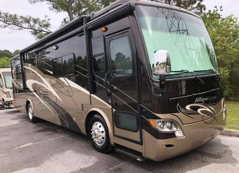 Two-tone beige and black luxury motorhome parked outdoors with trees in background