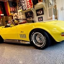 Bright yellow vintage sports car displayed in a garage with vintage signs and memorabilia in the background