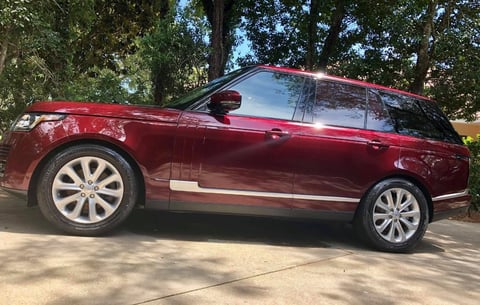 Red luxury SUV parked on driveway with silver alloy wheels and trees in background
