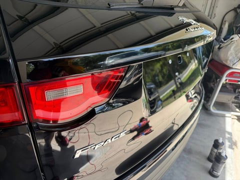 Close-up of a black and red vehicle tailgate showing chrome trim and reflection of surroundings under a canopy