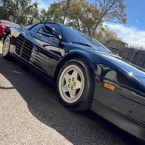Black sports car parked on asphalt with trees in background on a sunny day