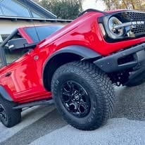 Red Ford Bronco SUV parked in driveway, side view showing black alloy wheels and modern design
