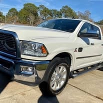 White pickup truck parked outdoors, featuring chrome details and a glossy finish with trees in the background