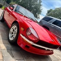 Red sports car parked on a driveway, front quarter view showing headlights and grille