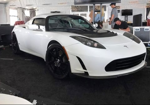 White Tesla Roadster convertible sports car on display in a showroom with staff in the background